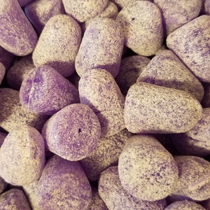 Puede incluir: Primer plano de un montón de caramelos morados con forma de pequeños conos redondeados. Los caramelos tienen una textura granulada y un tono morado claro.