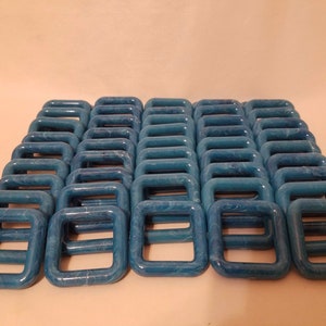 Könnte beinhalten: Eine Gruppe von 48 blauen D-Ringen aus Kunststoff. Die Ringe sind quadratisch mit abgerundeten Ecken und haben einen Marmoreffekt.
