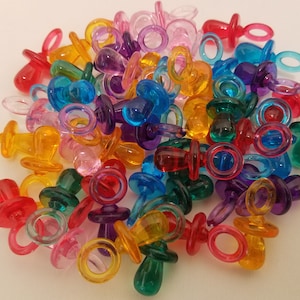 May include: A large pile of colorful plastic baby pacifier charms. The charms are in various colors, including red, orange, yellow, green, blue, purple, and pink.