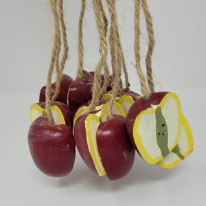 Pode incluir: Um grupo de oito maçãs de madeira pintadas de vermelho e amarelo. As maçãs são amarradas com um barbante e têm um estilo rústico, de fazenda.