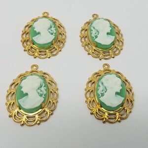 May include: Four oval pendants featuring a white profile cameo silhouette set against a light green background. Each cameo is encased in an ornate, gold-toned metal filigree frame with a small loop at the top for attachment to jewellery or crafts.