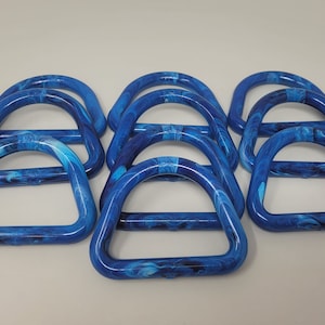 以下が含まれることがあります： 大理石模様の青いプラスチック製のDリングが10個。リングは積み重ねられています。