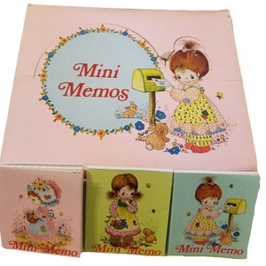 May include: A set of three mini memo pads with a pink, green, and blue background. Each pad features a cartoon girl with a mailbox and the text "Mini Memo".