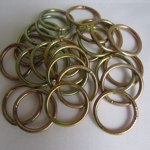 May include: A pile of gold-colored metal rings. The rings are all the same size and shape, and they are arranged in a random pattern.