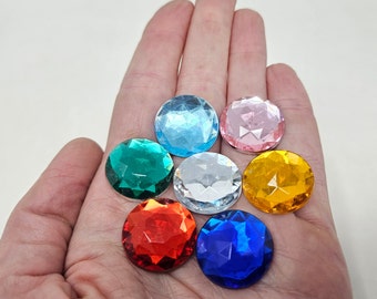 Puede incluir: Siete gemas redondas, facetadas e iridiscentes de varios colores, incluyendo azul, verde, rosa, amarillo, rojo y transparente, mostradas en una mano.