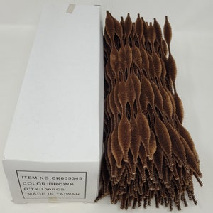 May include: A box of brown craft supplies, with a quantity of 100 pieces. The items are a dark brown colour and have a textured, fuzzy appearance. The box is white with printed text.