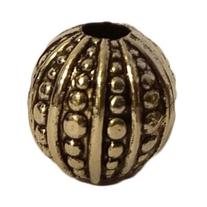 May include: A gold-toned metal bead with a textured surface. The bead has a round shape and is decorated with raised dots and lines.
