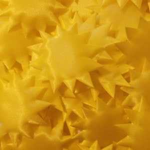 May include: A close-up of a pile of yellow fabric star shapes. The stars are made of a soft, silky material and have a slightly textured surface.