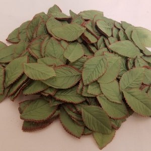 May include: A pile of green fabric leaves with a reddish-brown trim. The leaves have a detailed veining pattern and a slightly textured surface. These artificial leaves are likely for crafting or decorative purposes.