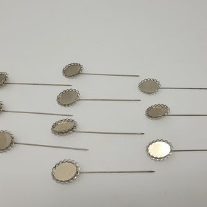 May include: Ten silver oval-shaped settings with a decorative edge and a pin attached. The settings are for making jewelry or crafts.