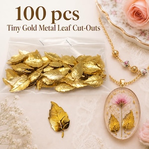 Puede incluir: Una bolsa de plástico transparente que contiene 100 piezas de pequeñas hojas de metal dorado recortadas, con una hoja dorada suelta colocada junto a la bolsa. El texto 100 pcs Tiny Gold Metal Leaf Cut-Outs está impreso en marrón sobre la bolsa.