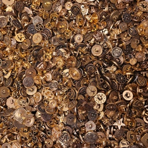 May include: A large collection of gold-toned metal buttons of various shapes and sizes. The buttons have intricate designs and are perfect for crafting and sewing projects.