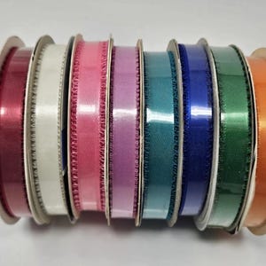 May include: Spools of colorful satin ribbon in various shades, including red, white, pink, purple, teal, blue, green, and orange. Each spool has a decorative edge and is ready for crafting or gift wrapping.