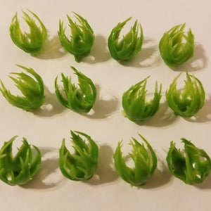 May include: Twelve green plastic flower buds with a spiky, textured design. The buds are arranged in four rows of three.