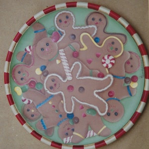 May include: A round plate with a red and white border features a festive design of gingerbread men and women. The plate is decorated with candy and icing details.
