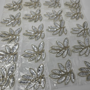 May include: A collection of silver leaf-shaped embellishments with sequins, ideal for adding sparkle to clothing or crafts.
