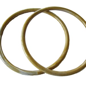 May include: Two wooden rings, one slightly larger than the other, are interlocked. The rings are a light brown color with a subtle white marbling effect.