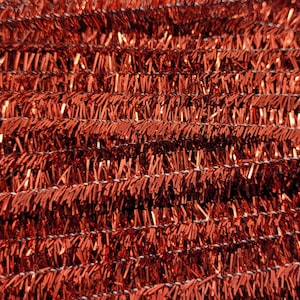 May include: Close-up of a textured, reddish-brown tinsel material. The tinsel is arranged in horizontal rows, with a metallic sheen. The texture is rough and irregular, creating a shimmering effect. The background is out of focus.
