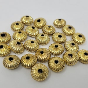 以下が含まれることがあります： フルーテッドデザインの金色の金属ビーズ20個のグループ。ビーズの中央には、糸を通すための小さな穴があります。