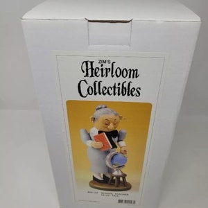 May include: A Zim's Heirloom Collectibles figurine of a school teacher, holding a book and a globe. The figurine is wearing a light blue dress and a black bow tie. The figurine is 12.5 inches tall.