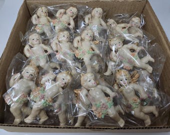 Puede incluir: Una caja de 15 adornos de ángel de porcelana blanca con detalles florales. Los ángeles tienen alas y sostienen flores. Los adornos están empaquetados en bolsas de plástico individuales.