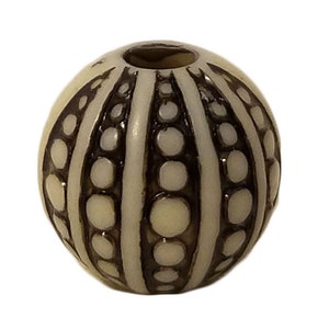 May include: A white bead with a brown and white striped pattern. The bead has a round shape and a smooth surface.