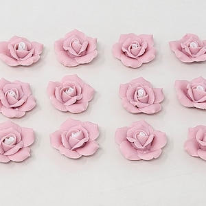 Könnte beinhalten: Zwölf rosafarbene Keramikrosen mit weißen Zentren. Die Rosen sind in vier Reihen zu je drei angeordnet.