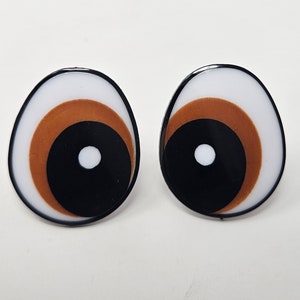 May include: A pair of white, brown, and black googly eyes with a white center. The eyes are oval shaped and have a glossy finish.