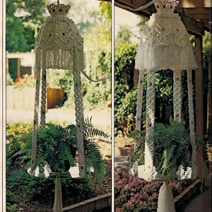 May include: Two white macrame plant hangers with a white tassel hanging from the bottom. The hangers are hanging from the ceiling and have a plant in each one. The plants are green and leafy. The hangers are in a garden setting.