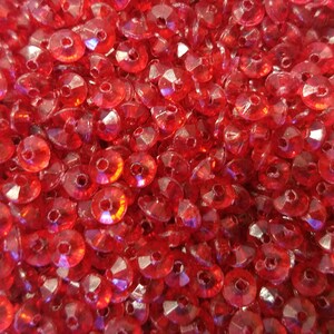 May include: A large collection of small, circular, translucent red beads. Each bead features a faceted surface that reflects light, creating a sparkling effect. The beads are arranged in a dense, overlapping pile, showing a consistent vibrant red color throughout the entire group of individual craft components.