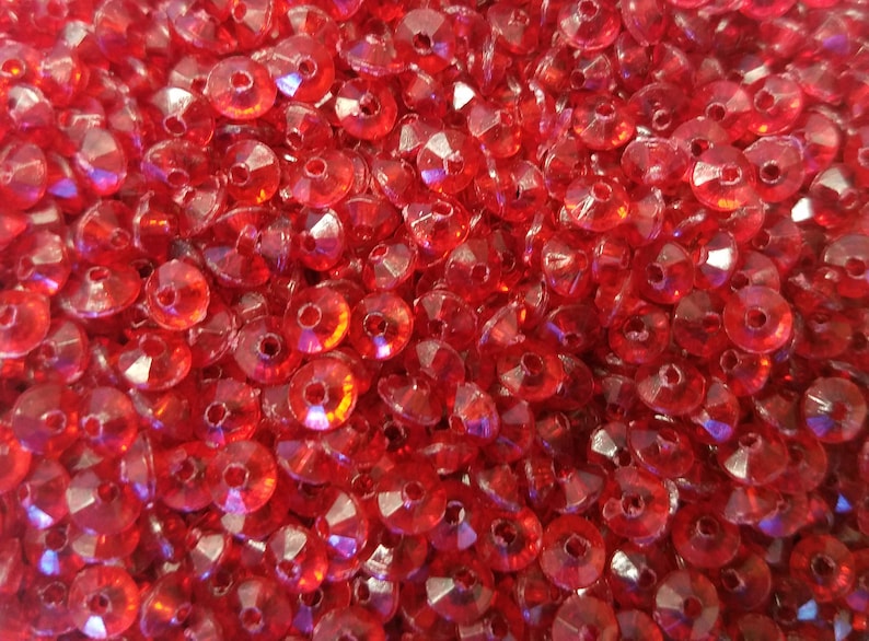 May include: A large collection of small, circular, translucent red beads. Each bead features a faceted surface that reflects light, creating a sparkling effect. The beads are arranged in a dense, overlapping pile, showing a consistent vibrant red color throughout the entire group of individual craft components.