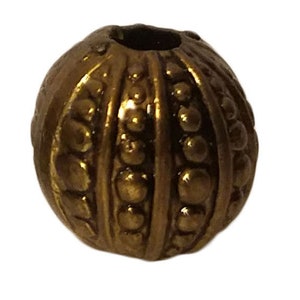 May include: A gold-toned metal bead with a textured surface. The bead has a round shape and is decorated with raised dots and lines.