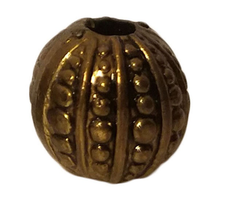 May include: A gold-toned metal bead with a textured surface. The bead has a round shape and is decorated with raised dots and lines.