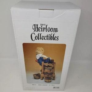 May include: A white box with a picture of a figurine of a person operating a wooden wine press. The box is labeled "Zim's Heirloom Collectibles" and "200-31 Wine Maker 12" Tall".
