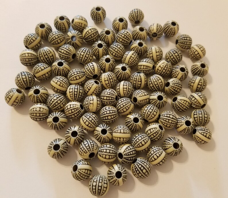 May include: A large group of off-white round beads with a black and white striped pattern. The beads are about 1 inch in diameter.