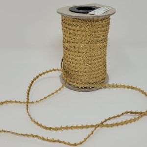 May include: A spool of gold metallic trim with a textured, jagged edge. The trim is wound around a cardboard spool with a black center.
