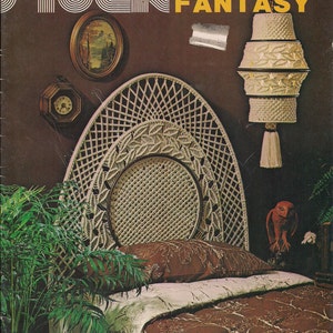 May include: A white macrame headboard with a brown and white patterned bedspread. The headboard is in the shape of a large teardrop and has a woven design. The bedspread has a floral pattern and is tucked into the bed. The image also includes a macrame hanging lamp and a small plant in a pot.