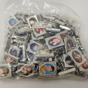 Könnte beinhalten: Ein klarer Plastikbeutel gefüllt mit zahlreichen kleinen, silberfarbenen Anhängern. Jeder Anhänger zeigt ein kleines, farbenfrohes Bild in einem dekorativen Rahmen. Der Text "ITEM NO. 083601-1 QTY: 100 PCS MADE IN CHINA" ist auf einem Etikett zu sehen.