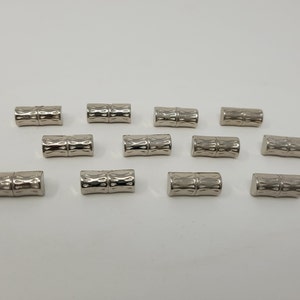 May include: A set of twelve silver metal cord end caps with a decorative pattern. The caps are designed to be used on the ends of cords to prevent fraying.