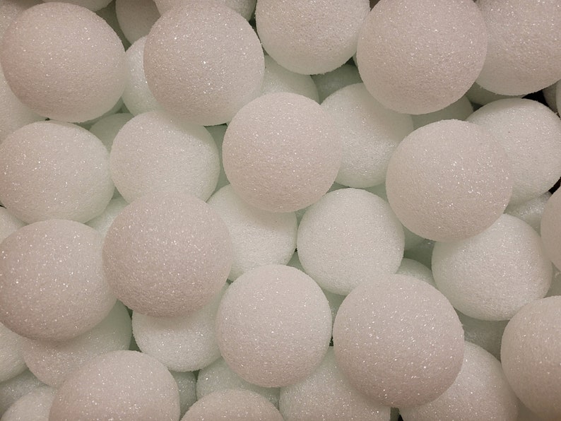 May include: A collection of numerous white, spherical foam balls with a textured, granular surface. Each ball is uniform in shape and size, creating a dense, repeating pattern of white circles that fill the entire frame of the image.