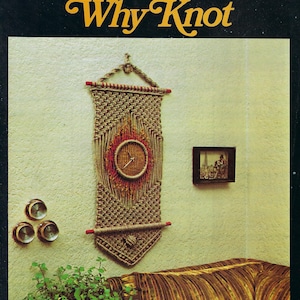 May include: A wall hanging with a clock, made of macrame, is the focal point of this image. The clock is surrounded by a circular design in red and brown. The text "Macrame Why Knot" is at the top. Other items include a small framed picture and three small round objects.