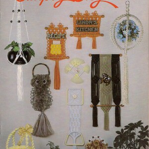 May include: A collection of macrame wall hangings and plant hangers in various colors and designs. The hangings feature geometric patterns, a recipe holder, and a sign that says "Linda's Kitchen". The image also includes a macrame owl, a basket, and a plant.