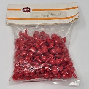 May include: A clear plastic bag filled with numerous small, red plastic fasteners. The fasteners have a mushroom-like shape with a rounded top and a stem. The bag's label reads "HDRF-10 RED 1GRS MADE IN JAPAN".