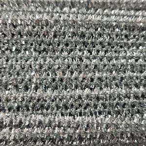 May include: Close-up of a silver fabric with a textured, woven pattern. The fabric has a metallic sheen and a slightly iridescent quality.