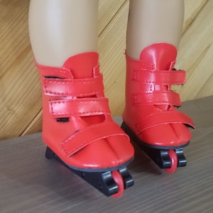 May include: A pair of red roller skates with black wheels and black straps. The skates are designed for dolls.