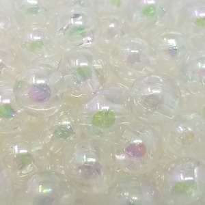 Puede incluir: Primer plano de un montón de cuentas blancas iridiscentes. Las cuentas son redondas y tienen una apariencia translúcida. Son perfectas para hacer joyas u otros artículos decorativos.