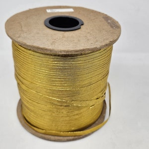 May include: A spool of gold ribbon. The ribbon is tightly wound around a cardboard core. The spool is made of cardboard and has a black plastic center. The ribbon is a bright, metallic gold color.