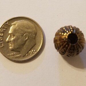 May include: A gold-toned metal bead with a decorative, textured surface. The bead has a hole in the center for stringing.