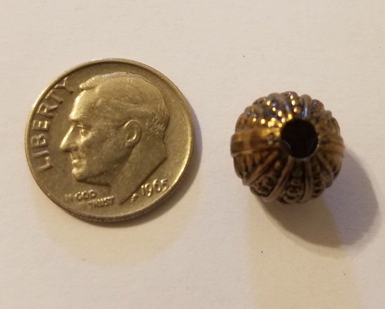 May include: A gold-toned metal bead with a decorative, textured surface. The bead has a hole in the center for stringing.