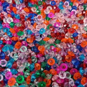 May include: A large collection of small, faceted plastic beads in a vibrant mix of translucent colors including red, orange, blue, green, pink, and clear. Each bead features a central hole and a multi-faceted surface that reflects light.